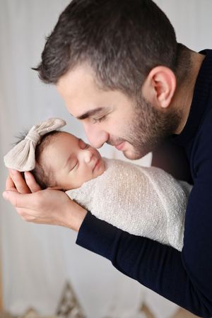 A tender moment with a sleeping newborn wearing a beige bow against a light background.
