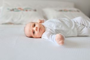 Baby wearing white sleepwear lying peacefully on white bedding with floral embroidery.