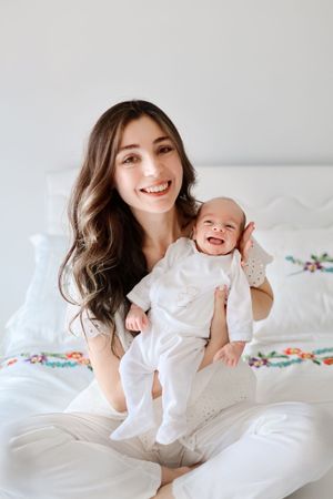 Joyful bonding moment between parent and baby dressed in white on a cozy bed.