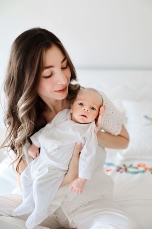 Intimate moment between parent and infant in white clothing on a bright bed.