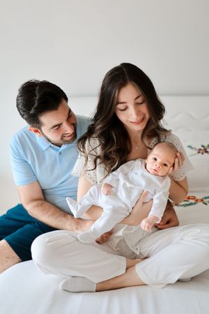 Happy family snuggling together on white bedding with their baby in matching outfits.