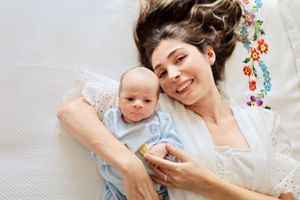 Parent and baby sharing a tender moment while lying on white bedding with floral details.