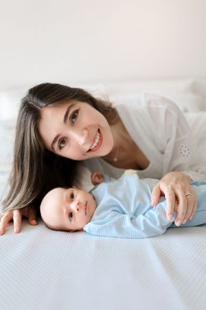 Tender moment between parent and baby lying side by side on white bedding.