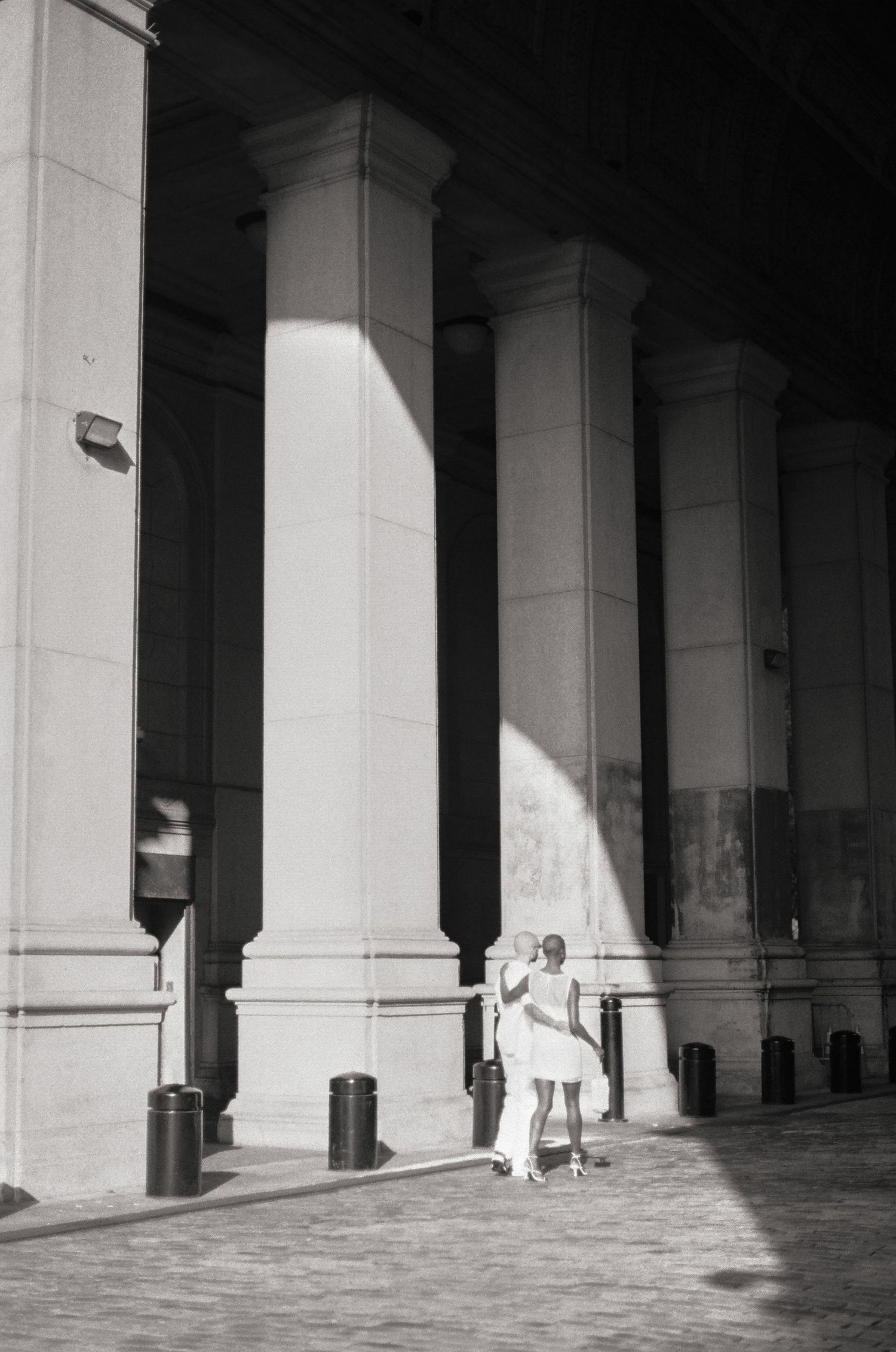 Figure in white dress poses between grand classical columns with dramatic shadows.