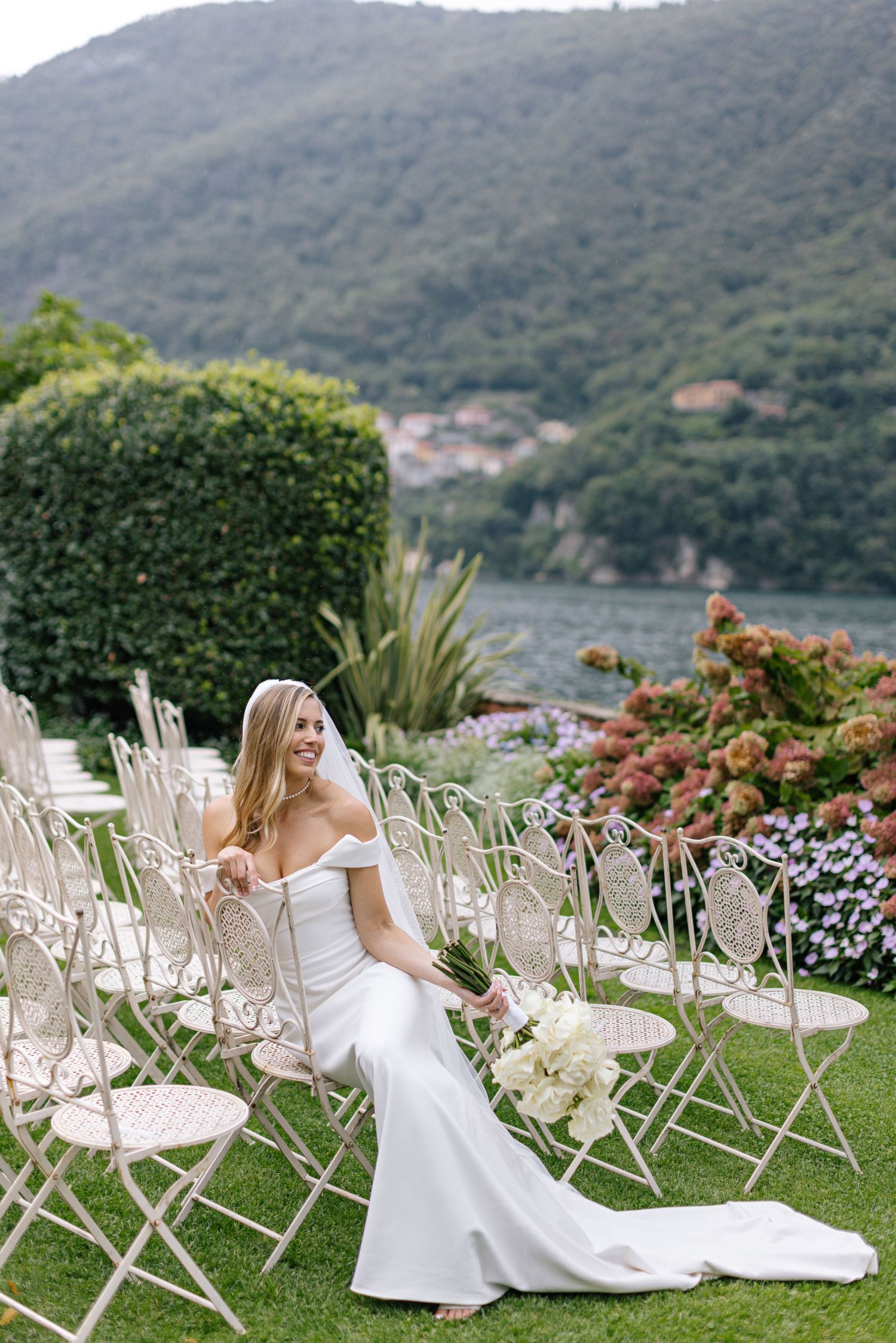 Scenic lakeside wedding setup with mountains and elegant white chairs overlooking the water.