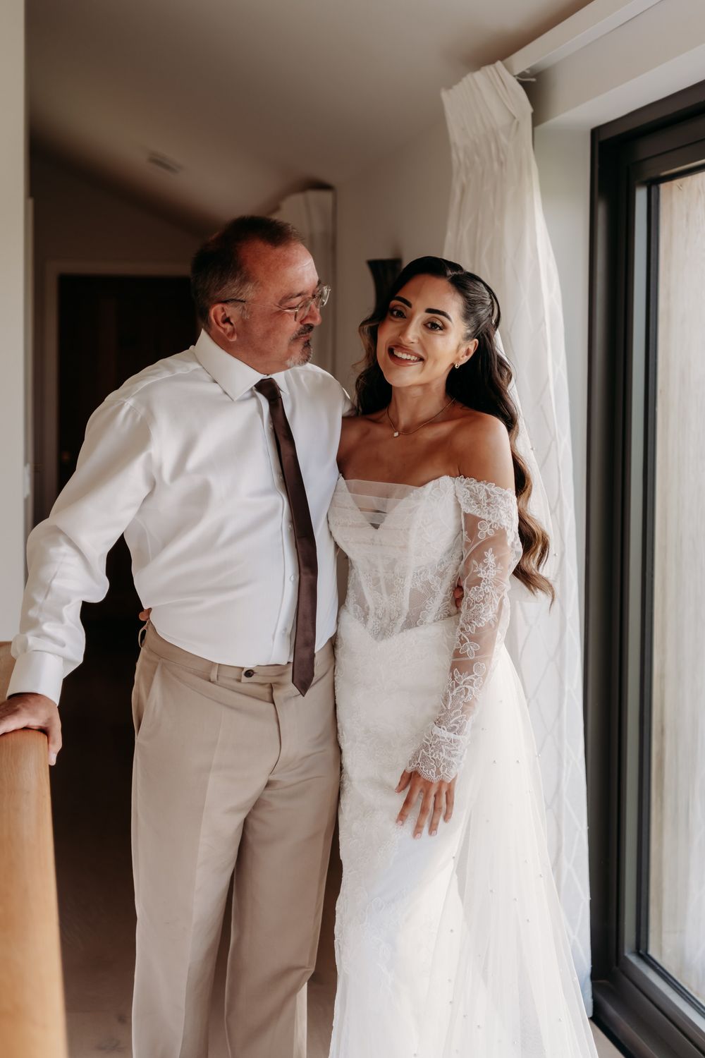 A wedding couple shares intimate candid moments in an all-white themed photoshoot by a window.