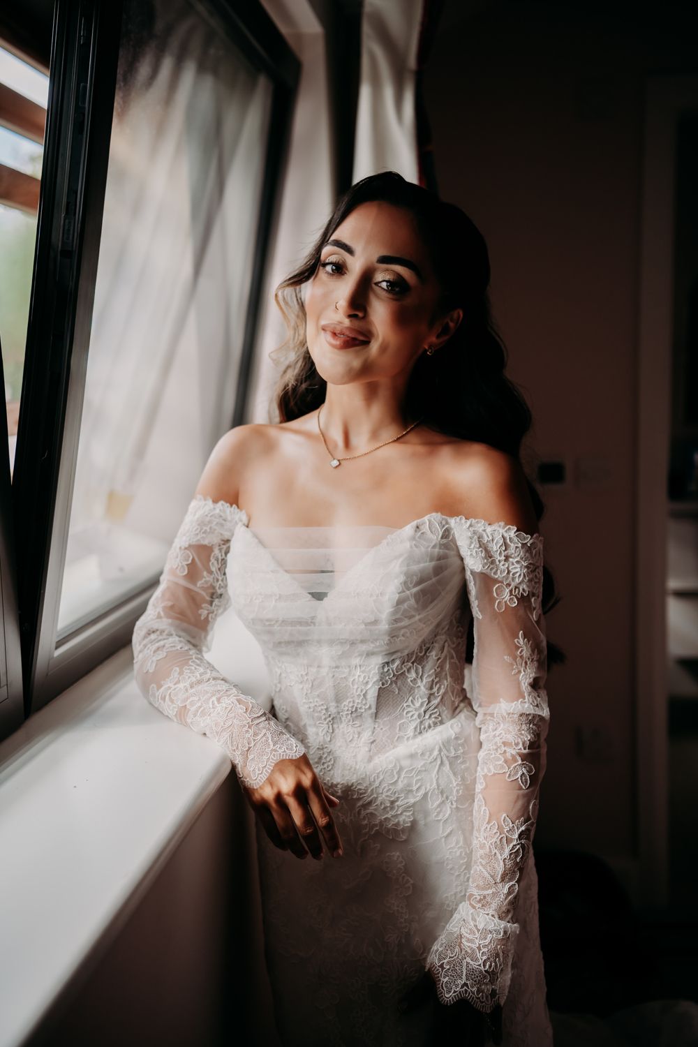 A series of moody bridal portraits showing a woman in a delicate lace gown by a window with natural light.