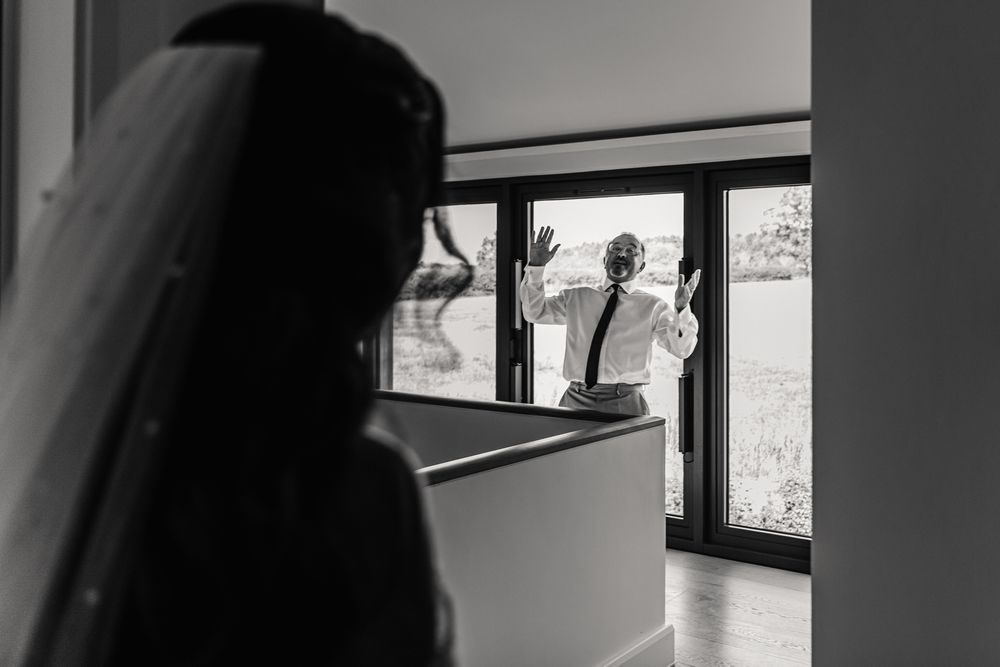 A silhouetted figure in a veil stands by a window while another person is visible through the glass in black and white.