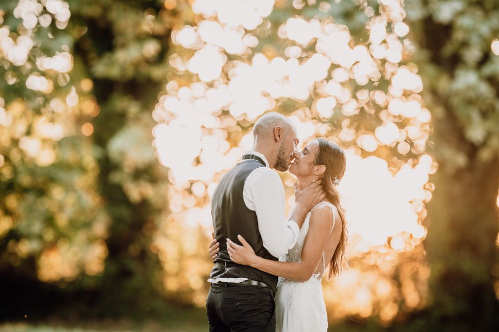 A couple shares a romantic kiss at sunset with glowing bokeh lights creating a heart shape in the background.