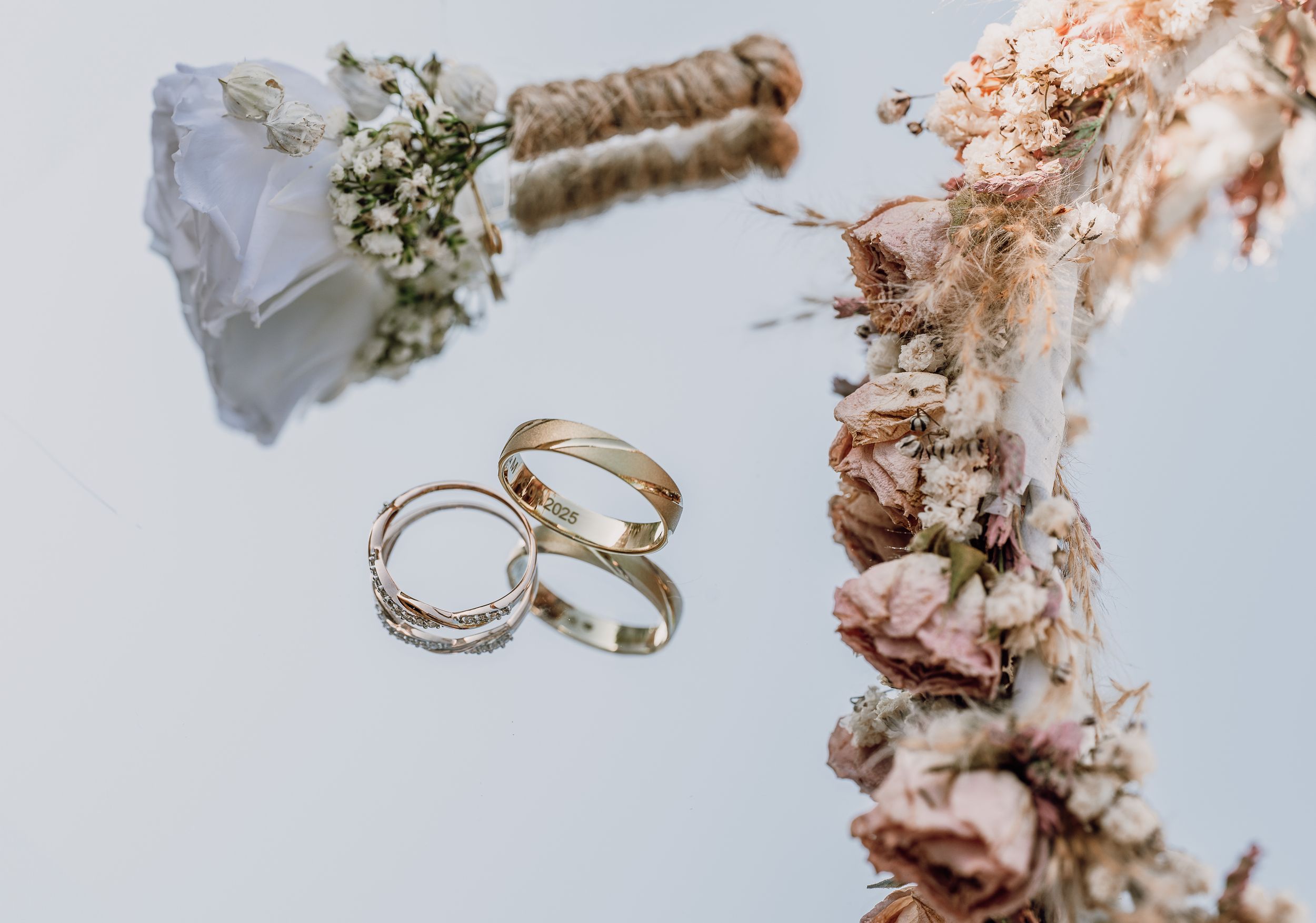 Wedding rings and a small white bouquet with baby's breath flowers arranged on a light background.