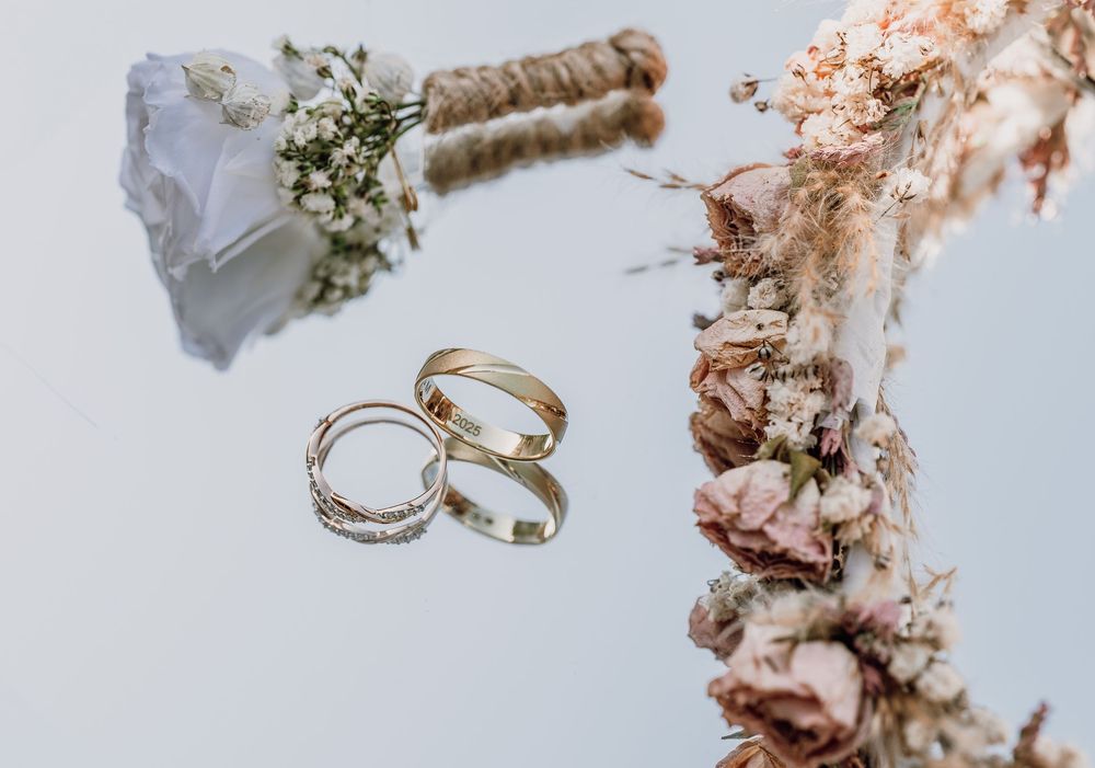 Wedding rings and a small white bouquet with baby's breath flowers arranged on a light background.