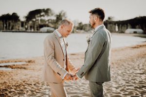 Couple sharing intimate moments on sunny beach in casual wedding attire.. photographe mariage lgbt Bordeaux gironde