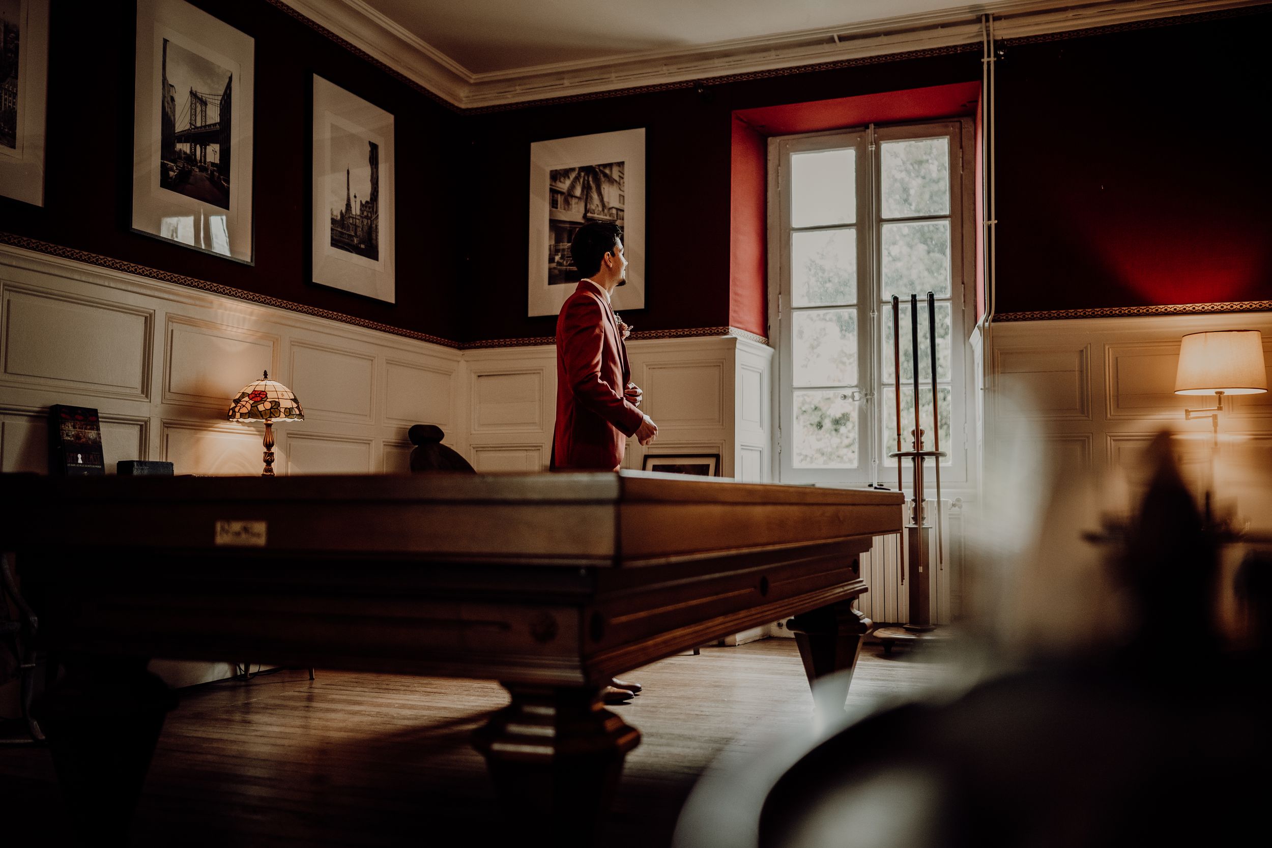 Silhouette of person in formal attire standing by window in dark room with pool table. photographe mariage Bordeaux, Gironde