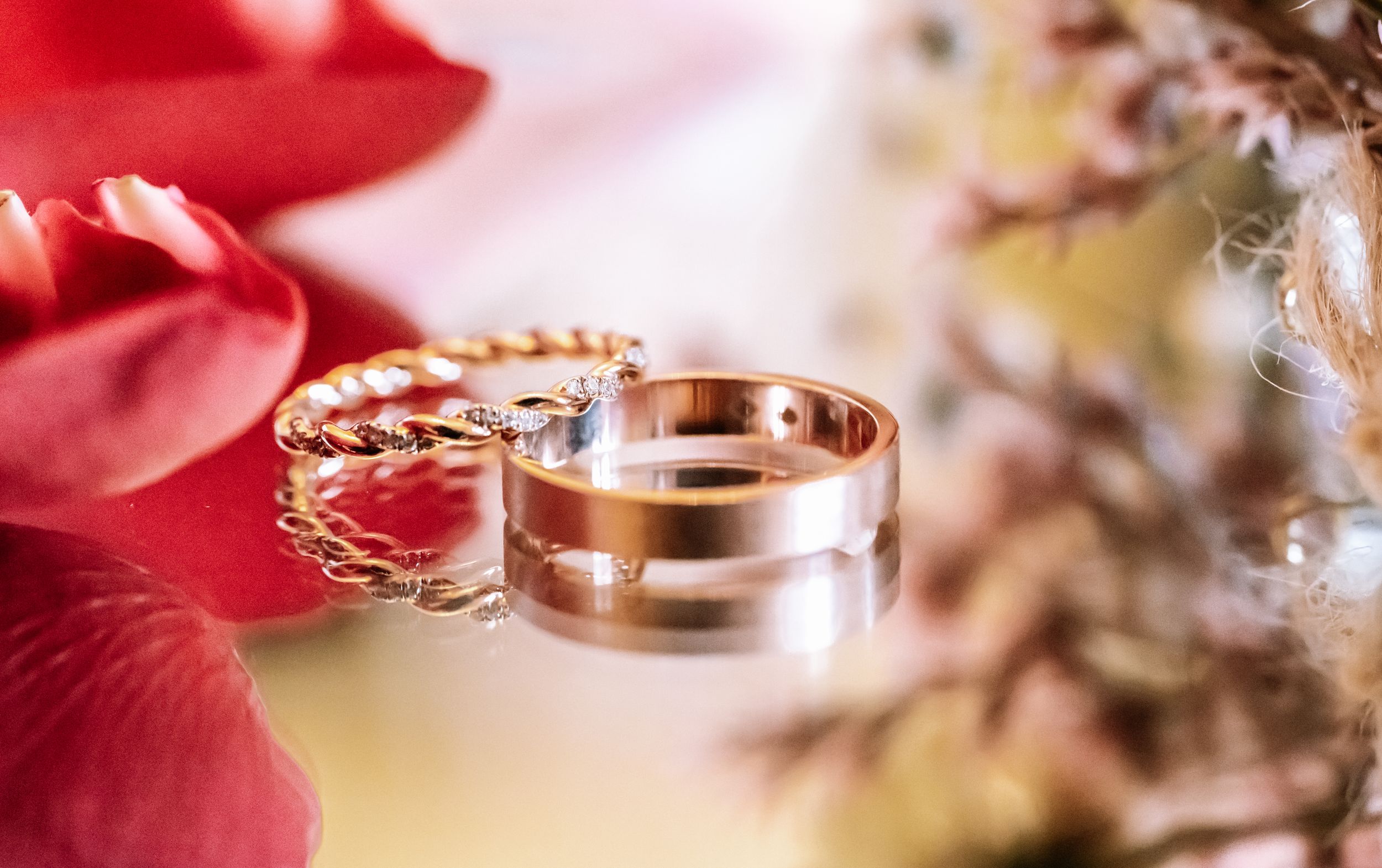 Wedding rings photographed with red flower petals in soft focus. photographe de mariage Bordeaux, Gironde
