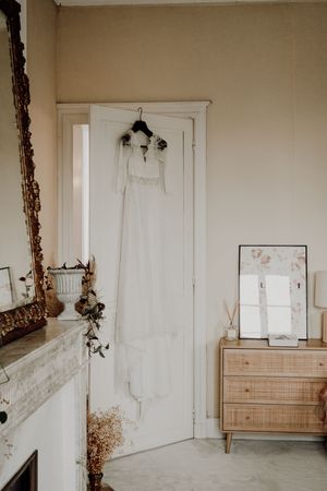 White wedding dress hanging on door in minimalist room with vintage furniture. photographe mariage Bordeaux, Gironde