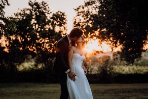 A couple embraces in a romantic sunset silhouette against a backdrop of trees and golden light.