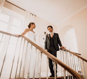 A bride and groom share a romantic moment on a white wooden staircase in warm lighting.