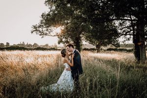 Romantic couple embracing in tall grass during golden hour sunset in a rustic outdoor setting.