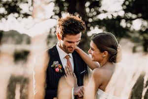 A happy couple embraces outdoors during golden hour on their wedding day, with soft sunlight filtering through trees.