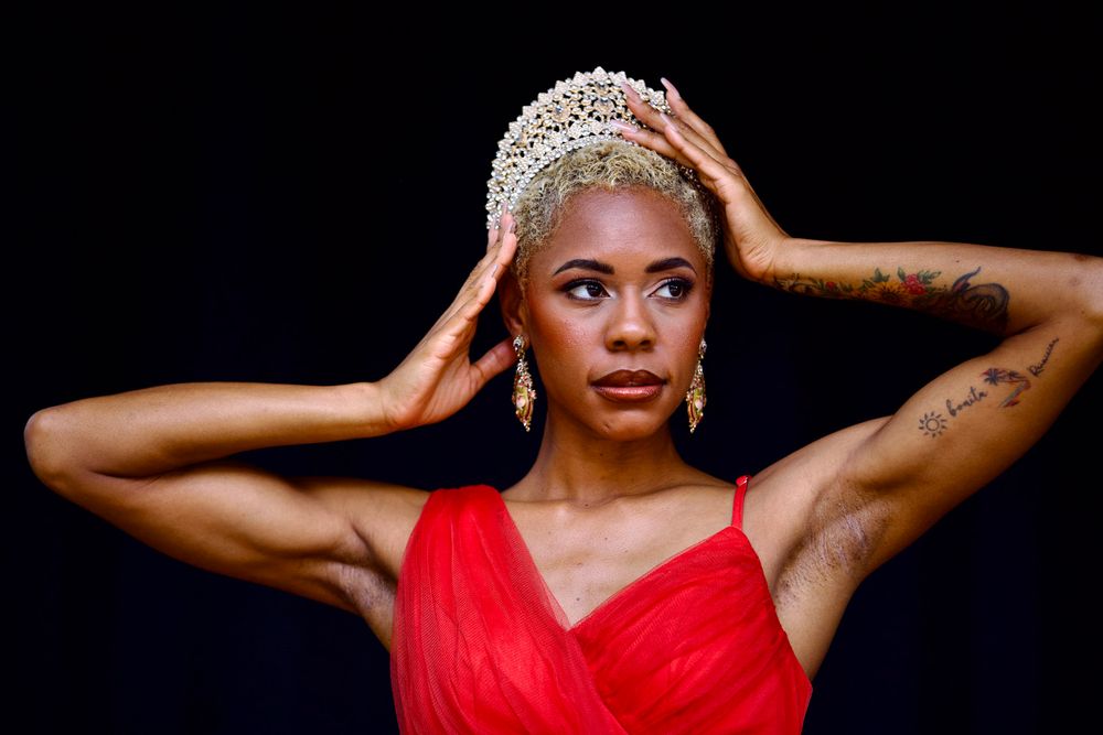 A glamorous portrait in red evening wear with a sparkling crown against a dark background.