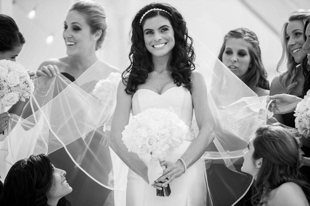 A black and white wedding photo showing a group joyfully gathered together with veils and white dresses.