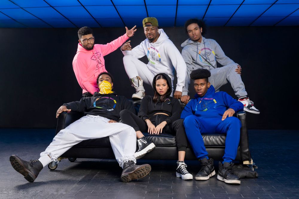 Group of dancers in casual streetwear poses together on black couch with blue lighting.