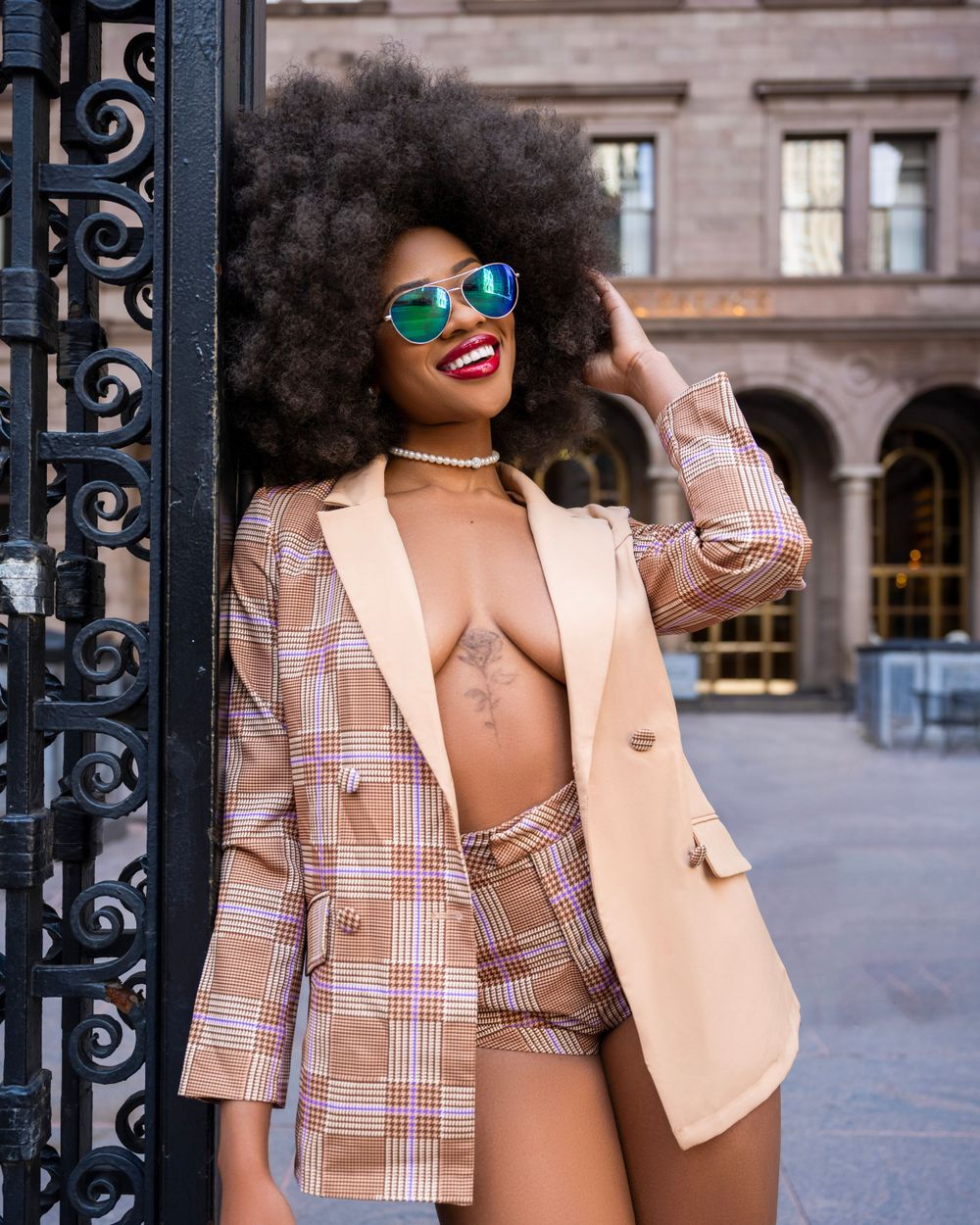 Street style photo featuring colorful sunglasses and plaid blazer in urban setting.