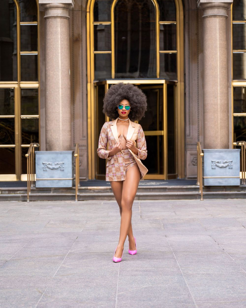 Fashion model in pink blazer and heels poses confidently against architectural backdrop.