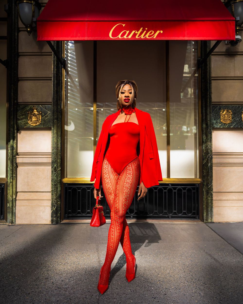 Bold red bodysuit and cape outfit photographed in front of Cartier store with dramatic lighting and urban backdrop.