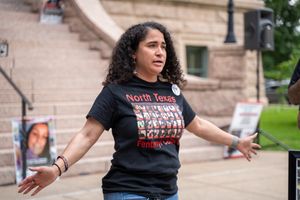 Activist speaking at outdoor rally wearing black t-shirt.