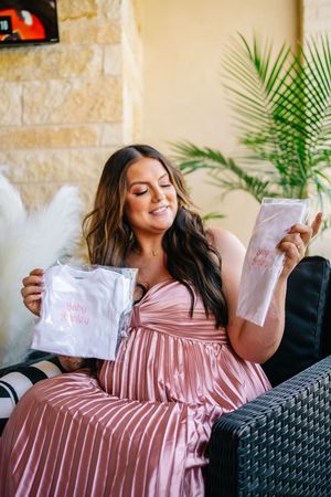 Person in pink striped dress holds baby shower gifts while sitting on outdoor furniture.