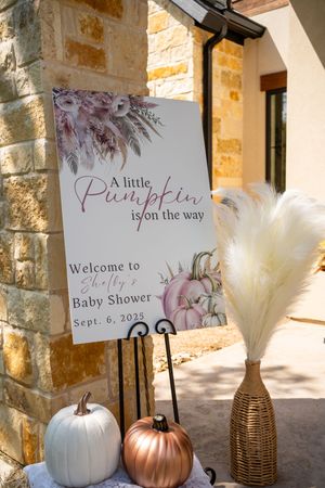 Autumn baby shower decorations featuring white and copper pumpkins with pampas grass in woven vases.