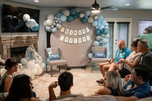 Friends and family gather at a blue-themed baby shower with balloon arch decorations.