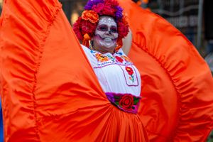 Performer in bright orange costume with red wig at festival or parade.