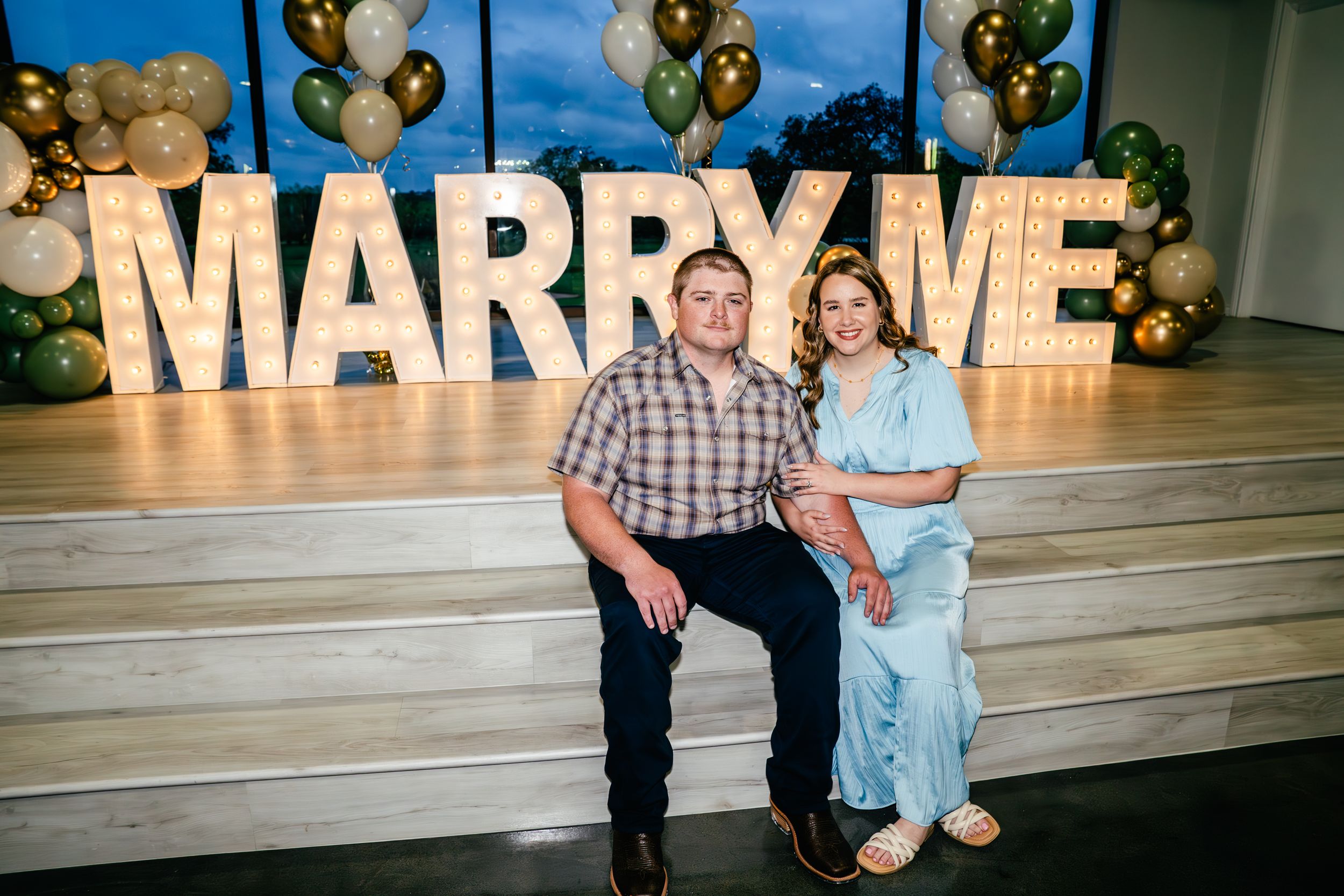 Event setup with gold and green balloon decorations against a blue backdrop with illuminated signage.
