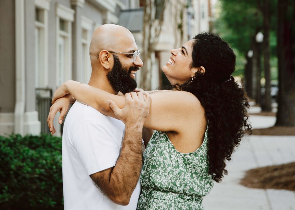 Couple laughs together during a playful moment on an urban sidewalk.