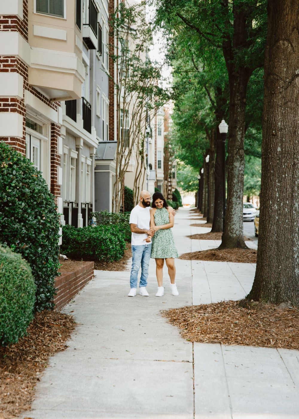 Couple walks hand in hand down a tree-lined sidewalk in an elegant neighborhood.