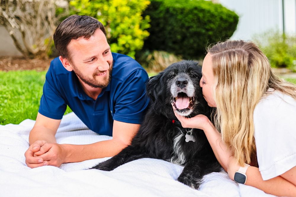 A candid image of a couple kissing their dog while laying on a blanket.