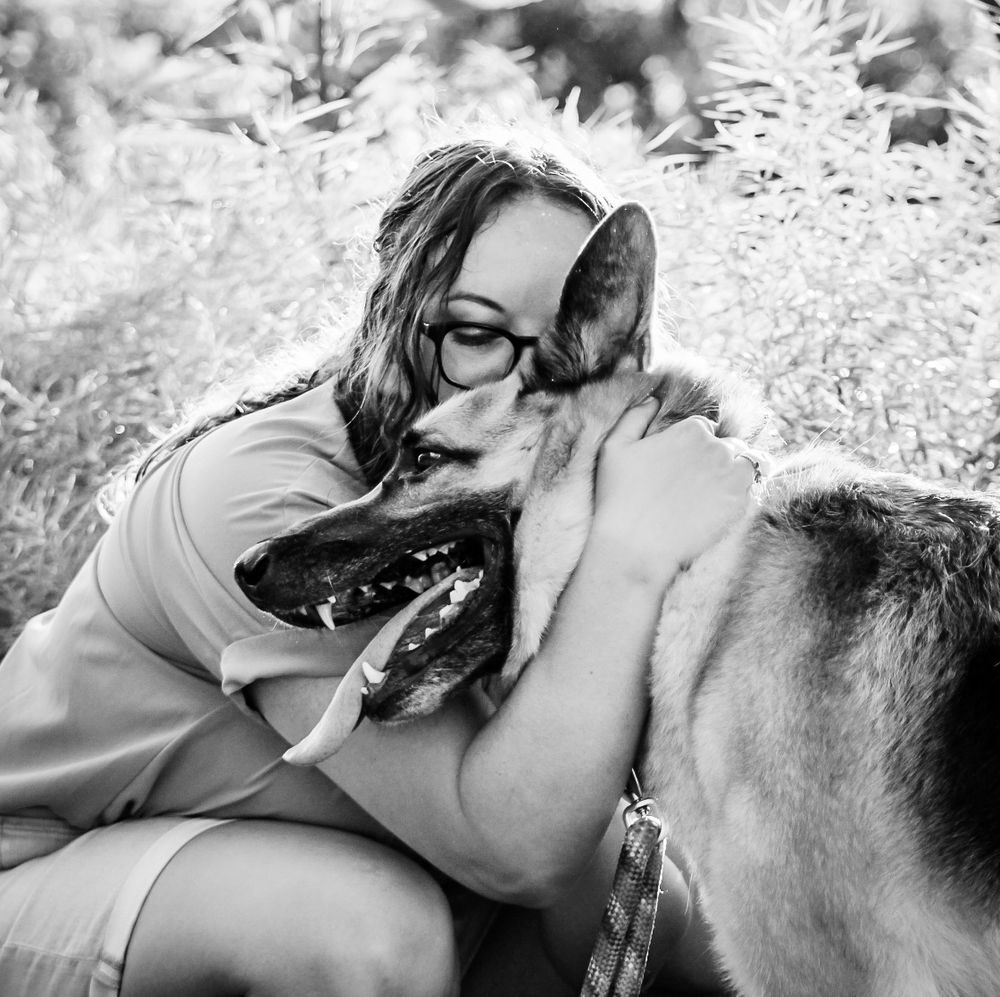 A candid black and white photo of a woman and hugging and kissing her dog.