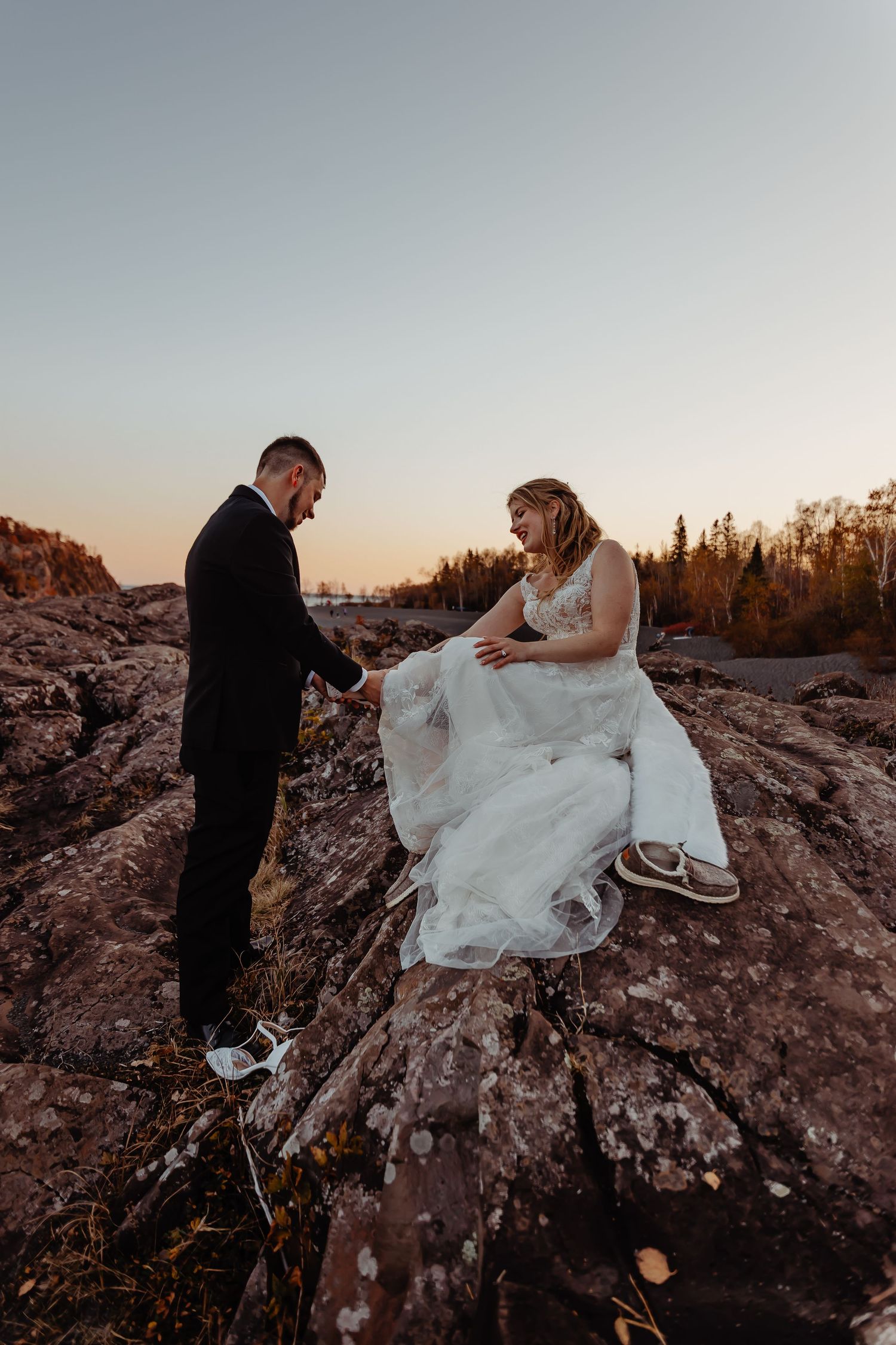 Wedding couple on rocky cliff during sunset with dramatic landscape.