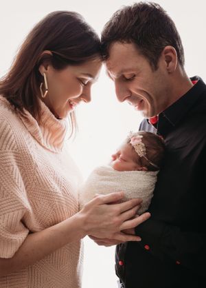 A peaceful family moment as parents in cozy sweaters lovingly gaze down at their swaddled newborn baby during newborn photos in Tampa