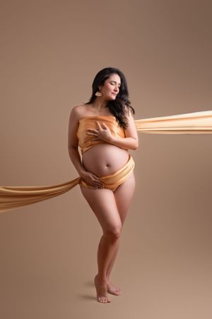 Artistic maternity photo with flowing gold fabric against neutral background showing an expectant mother during maternity photos in Tampa