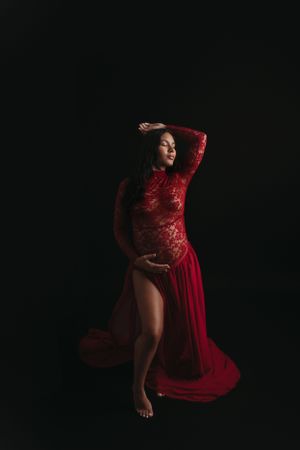 Dramatic maternity portrait of woman in flowing red lace gown against black background, Tampa Maternity Photography