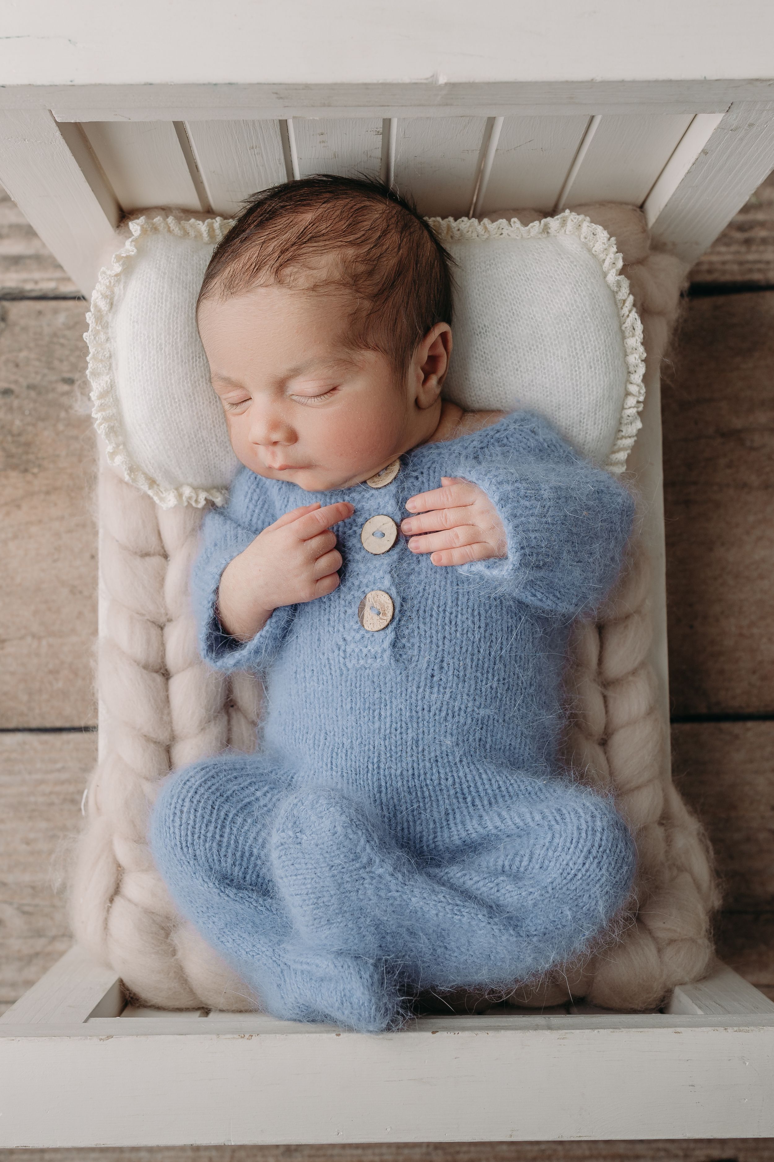 Newborn baby wearing soft blue knit romper sleeps peacefully on bed prop, perfect for newborn photography in Tampa