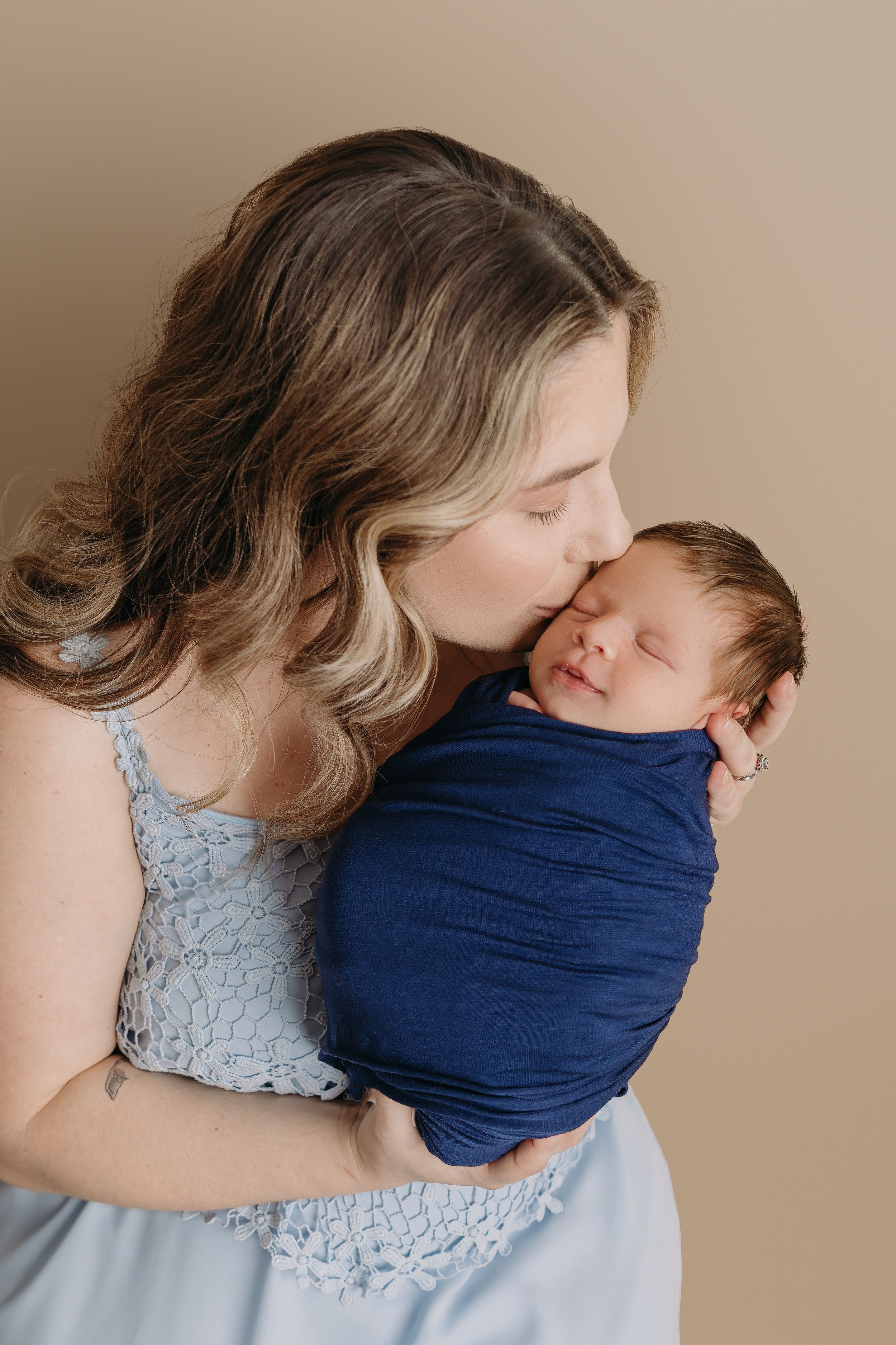 A tender moment between parent and newborn baby wrapped in navy blue cloth against a neutral background for Tampa newborn photos