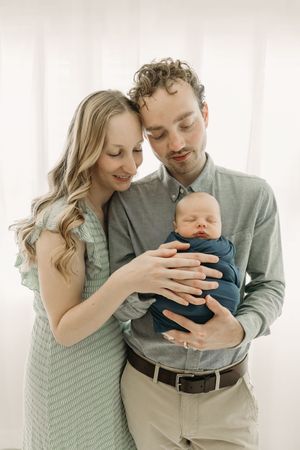 Parents in soft lighting holds their sleeping newborn baby while wearing mint green during Newborn photos in Tampa