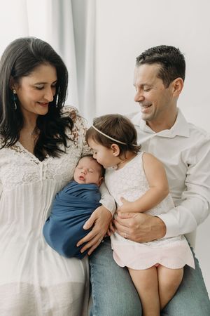 A family of four in casual white and blue outfits poses together lovingly during lifestyle newborn photos in Tampa