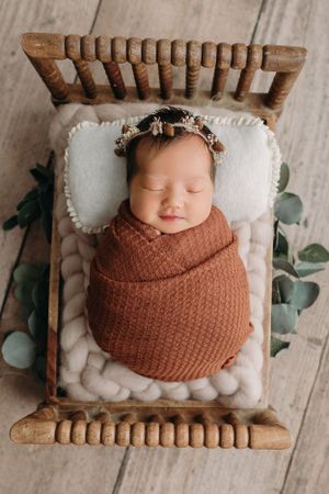 Sleeping newborn wrapped in rust knit blanket resting on wooden bed for Tampa Newborn Photography session