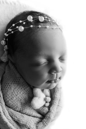 Sleeping newborn wrapped in soft gray blanket wearing delicate pearl headpiece in black and white portrait during Tampa Newborn Photography