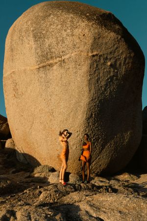 Two figures standing against massive boulder formation in sunset lighting.